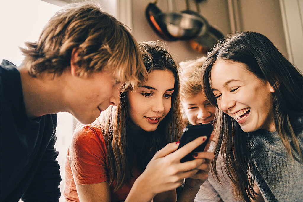 Eine Gruppe von Jugendlichen schaut gemeinsam auf ein Smartphone und lacht.