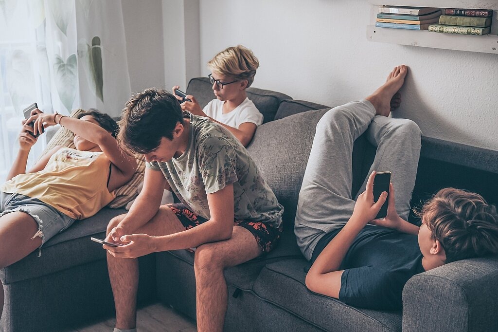 Jugendliche liegen und sitzen auf Sofa mit Smartphones