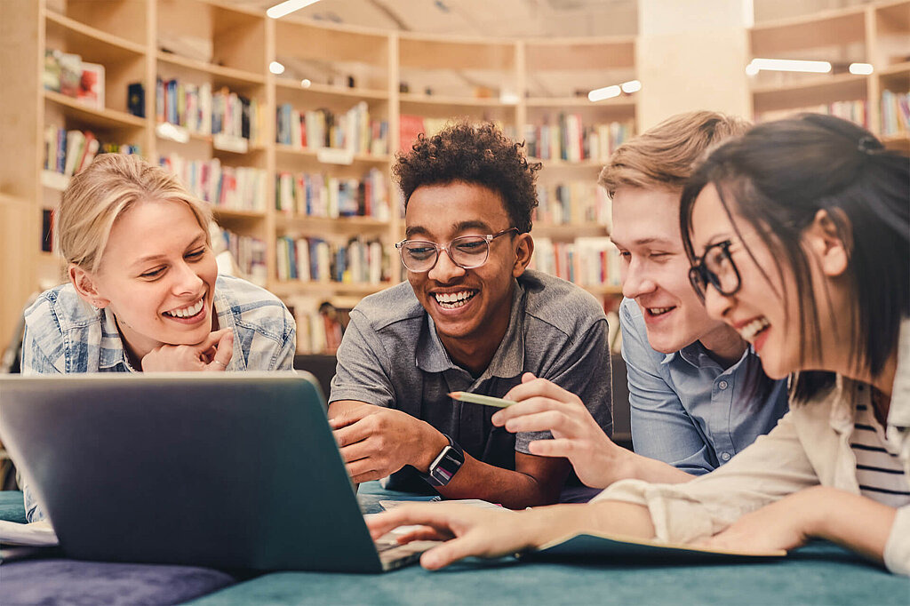 Vier Jugendliche sitzen vor einem Laptop und lachen.