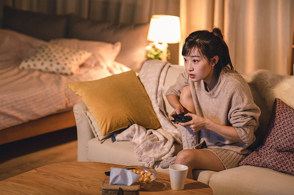 Mädchen sitzt auf der Couch und hält einen Controller zum Spielen eines Videospiels in der Hand.
