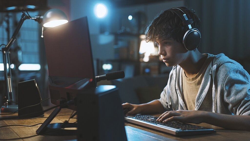 Jugendlicher spielt nachts mit Kopfhörern Computerspiele.