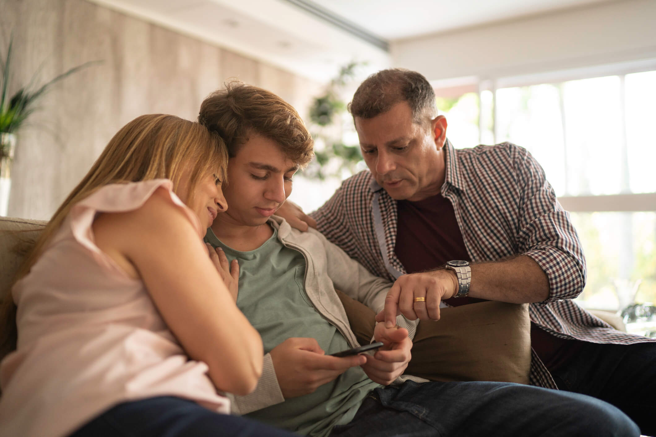 Eltern schauen mit Sohn zusammen auf Smartphone