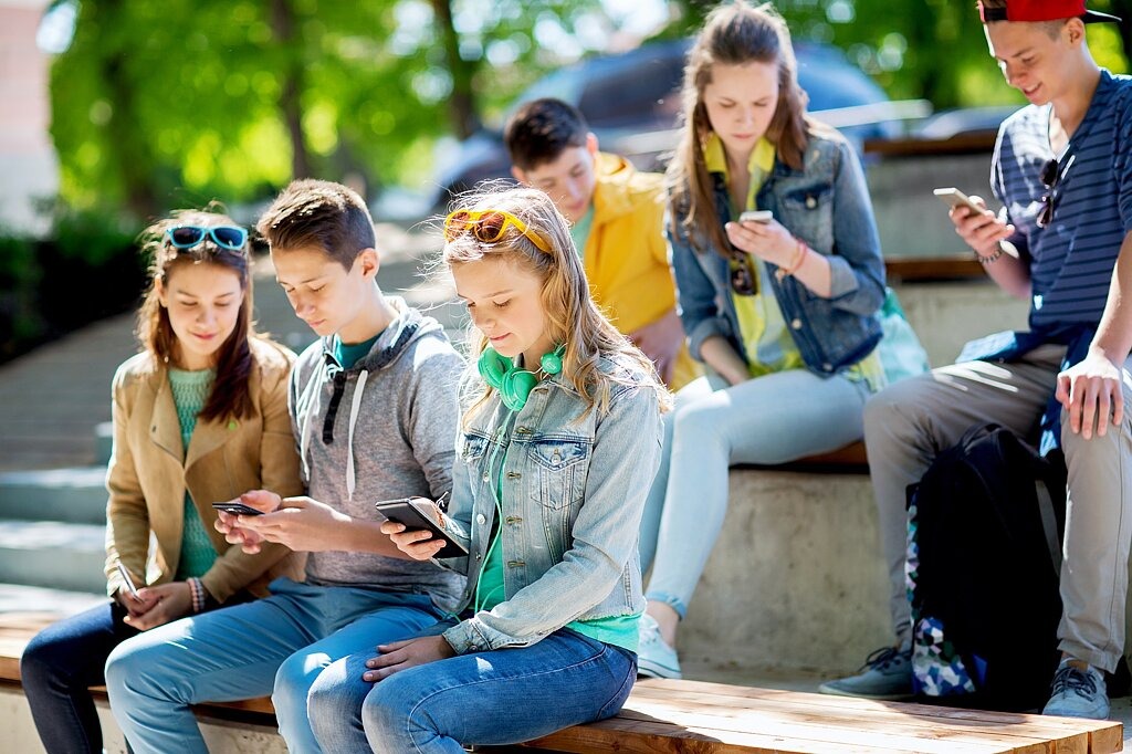 Schülerinnen und Schülern auf dem Schulhof schauen auf ihre Smartphones.