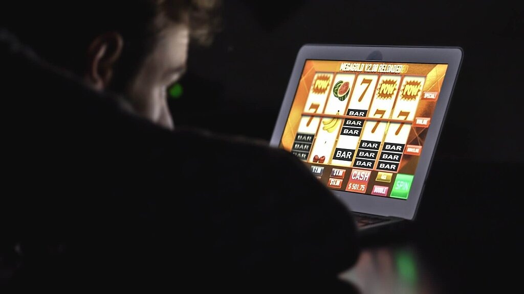 Junger Mann spielt an einem digitalen Spieleautomaten in einem dunklen Zimmer.