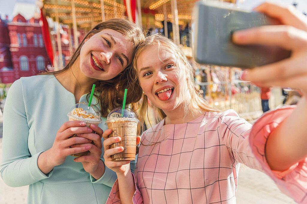 Zwei Mädchen machen ein Selfie mit Milchshake in der Hand.